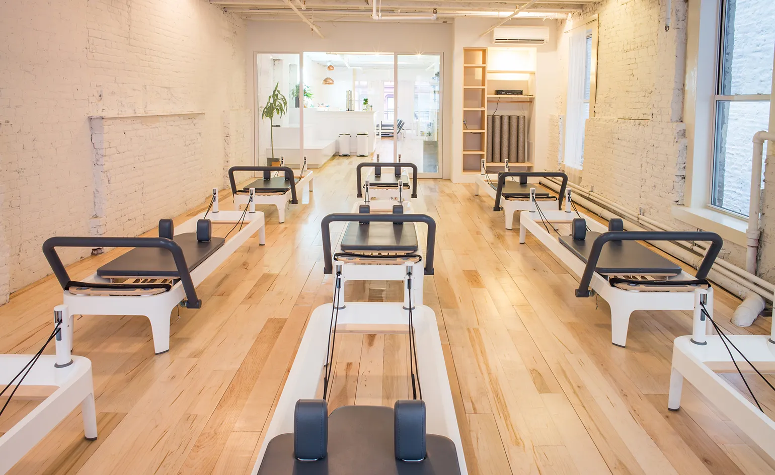 A bright, modern Pilates studio with wooden floors and white walls, featuring several reformer machines in rows, reflects the luxury Pilates Hamptons vibe—perfect for those seeking a premium Montauk reformer Pilates experience.